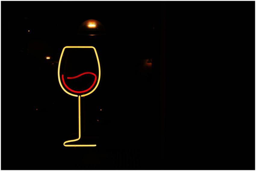 Stylish neon sign of wine glass on dark background
