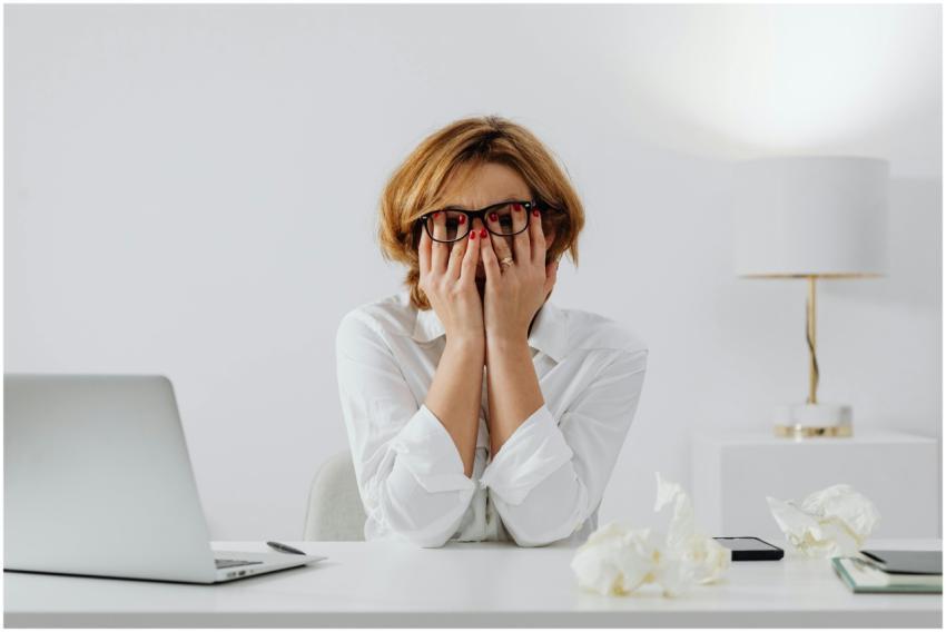 Woman with hands on face, sitting at desk with lap