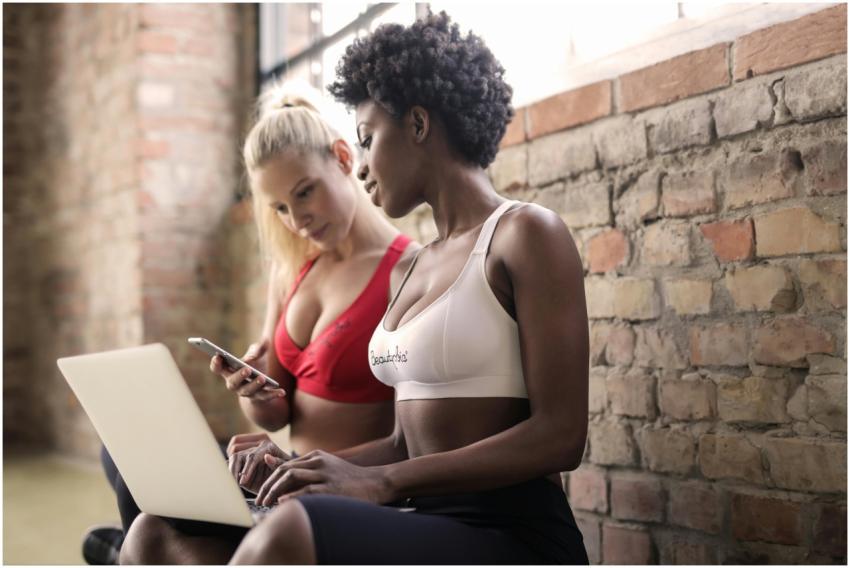 Two women in sportswear using a laptop and smartph