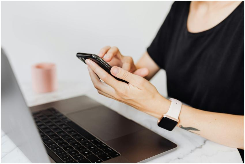 Close-up of a woman using a smartphone with a lapt