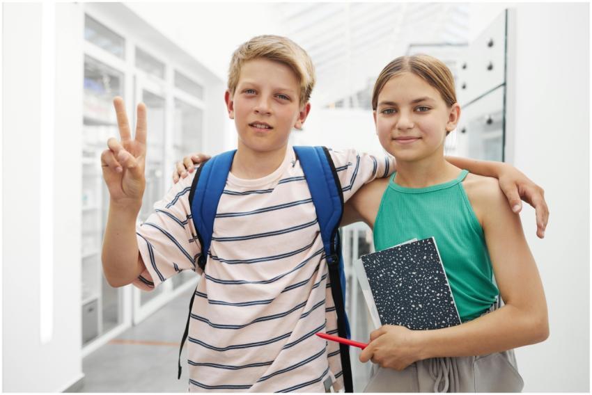 Two teenagers smiling in a school hallway, showing