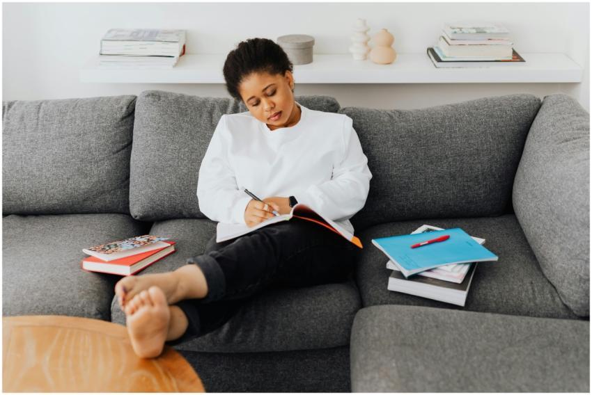 A young woman relaxes on a sofa, writing in a note