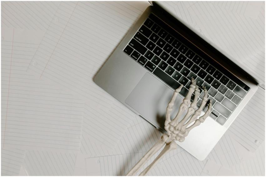Skeleton hand on laptop keyboard overlaid on paper