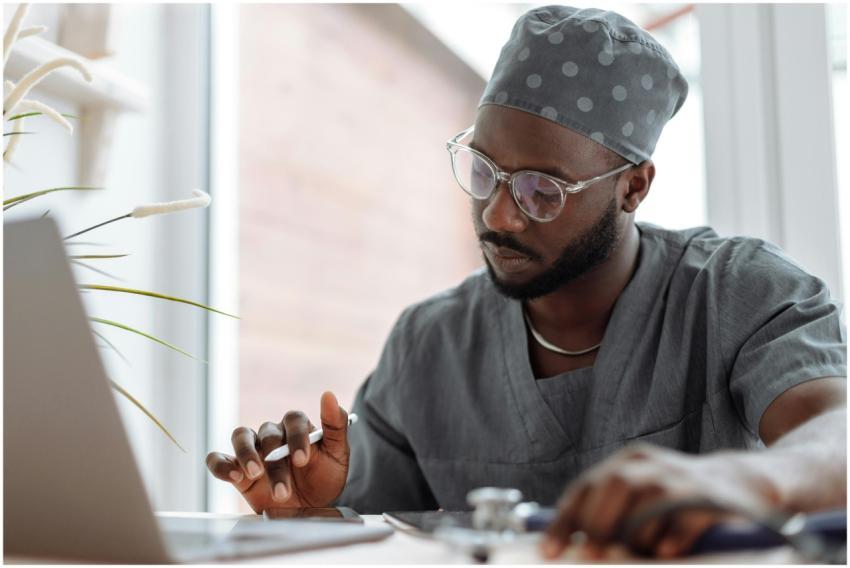 A focused male doctor in scrubs working on a lapto