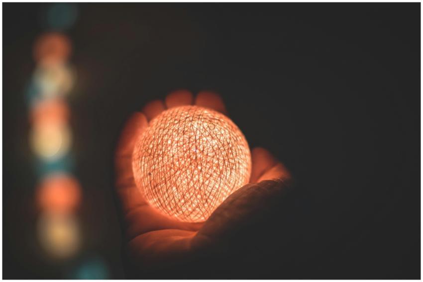 A warm illuminated sphere held by a hand in the da