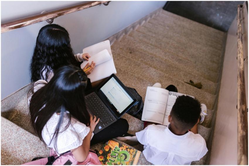 Three students sit on stairs, using laptops and no