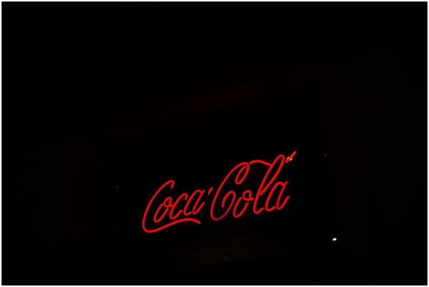 A bright neon Coca-Cola sign stands out against a