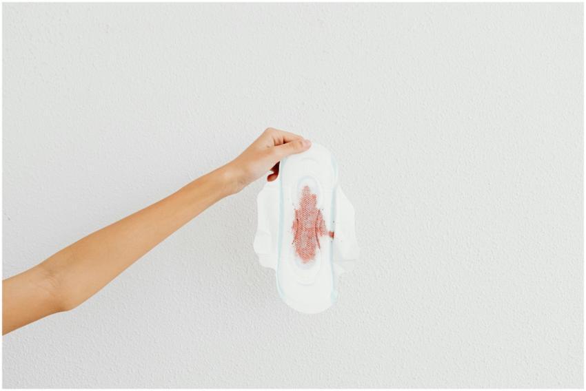 A hand holding a menstrual pad with blood stains,