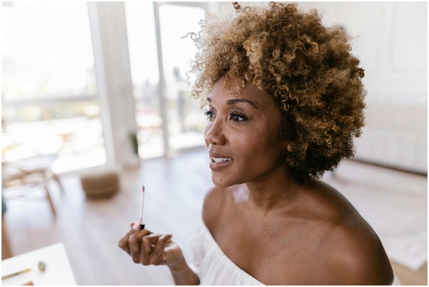 Confident woman with curly hair applying lipstick