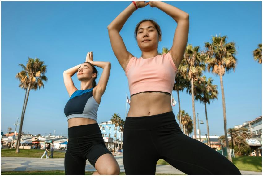 Two women practicing yoga poses outdoors, focusing