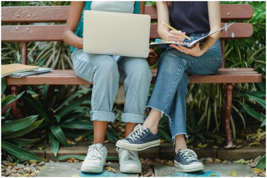 Two young women collaborating on a park bench with