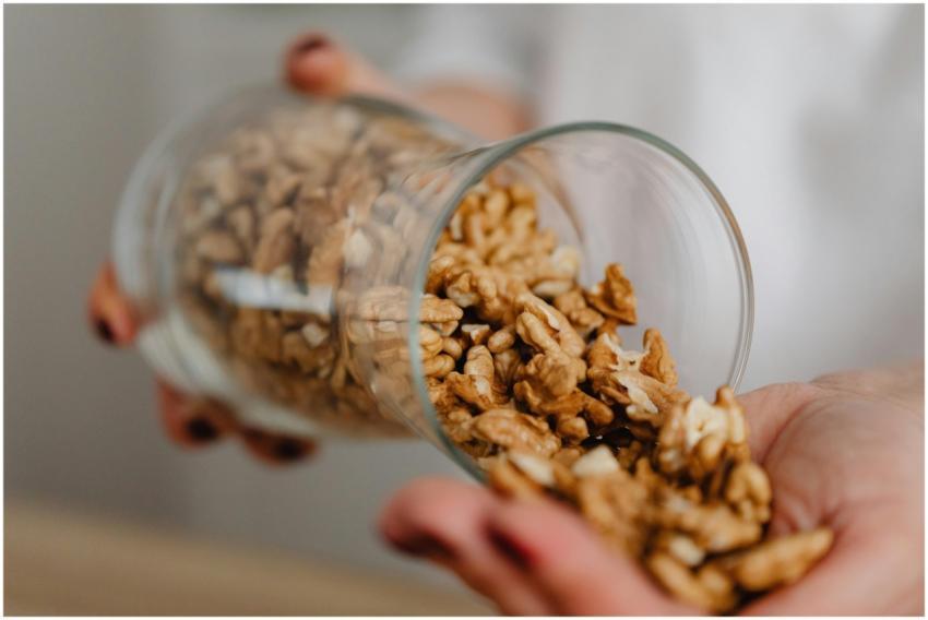 Hands pouring walnuts from a glass jar, featuring