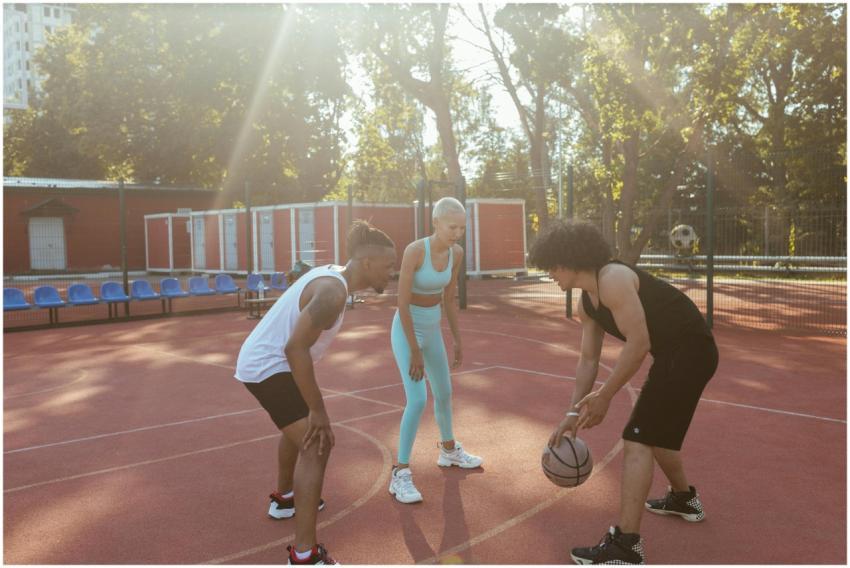 Three diverse young adults play basketball on an o