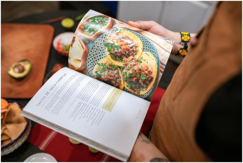 A person holding a cookbook open to a delicious ta