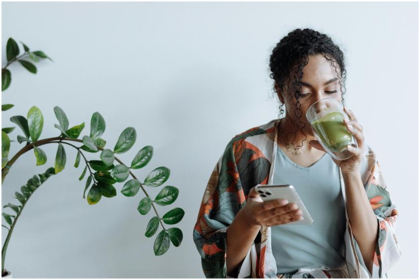 A woman sips matcha tea as she checks her phone, s