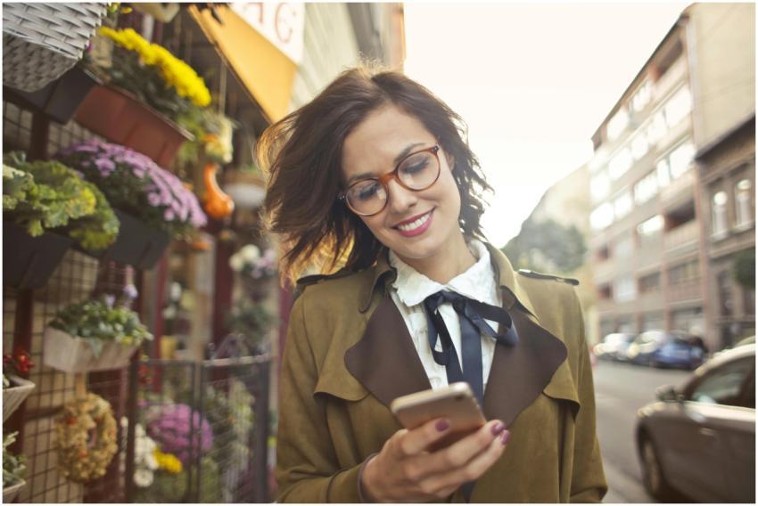 A smiling woman uses her phone outside a colorful