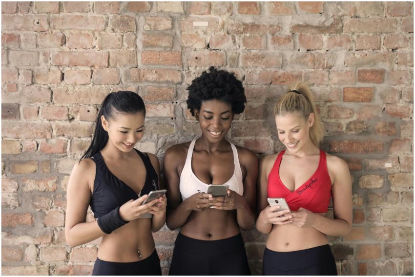Three diverse women smiling and using smartphones