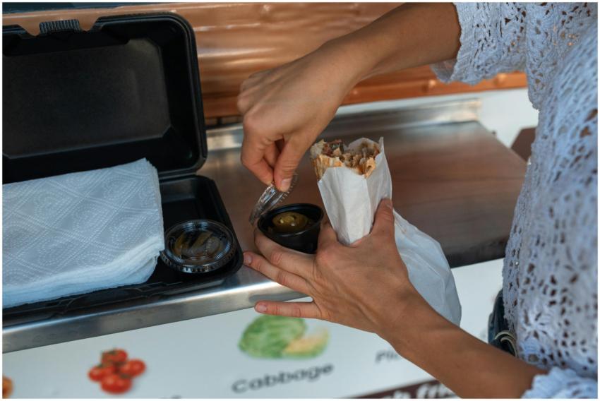 Person holding a shawarma with condiments, showcas
