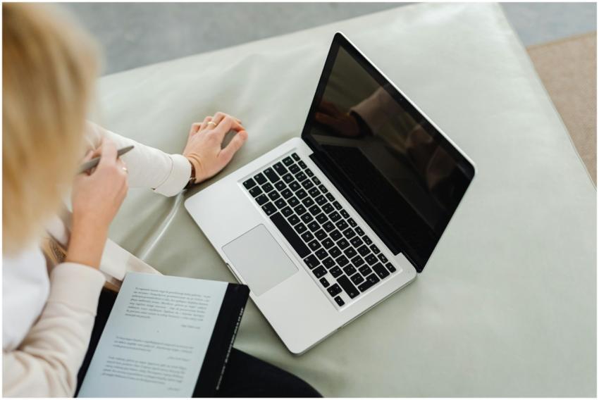 A woman using a laptop while taking notes indoors