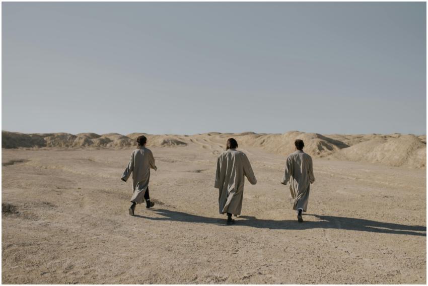 Three people wearing overcoats walking across an a