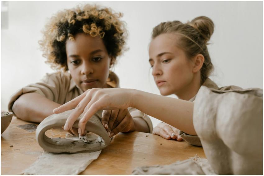 Two focused women crafting pottery pieces in a cre