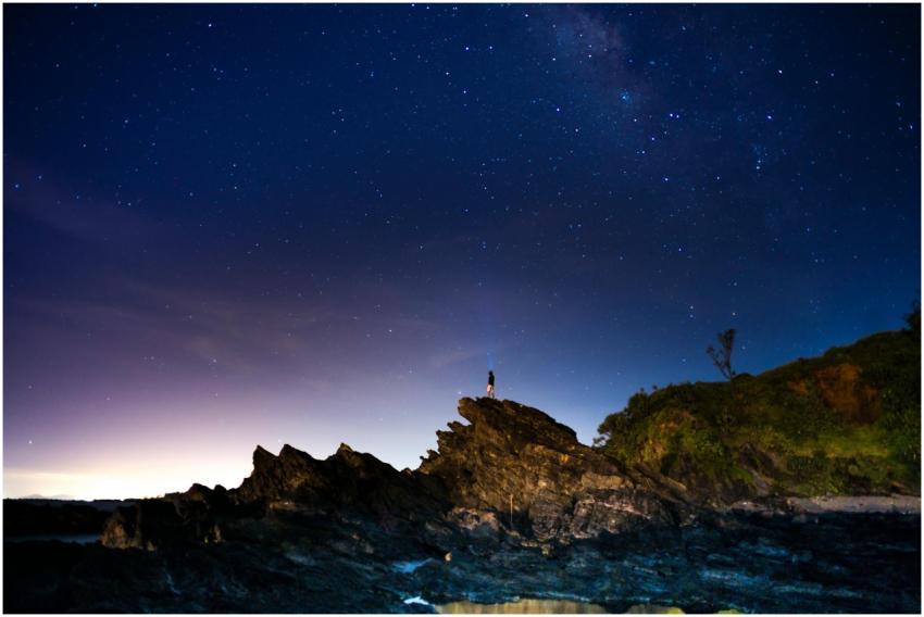 A lone person stands on rocky terrain beneath a st