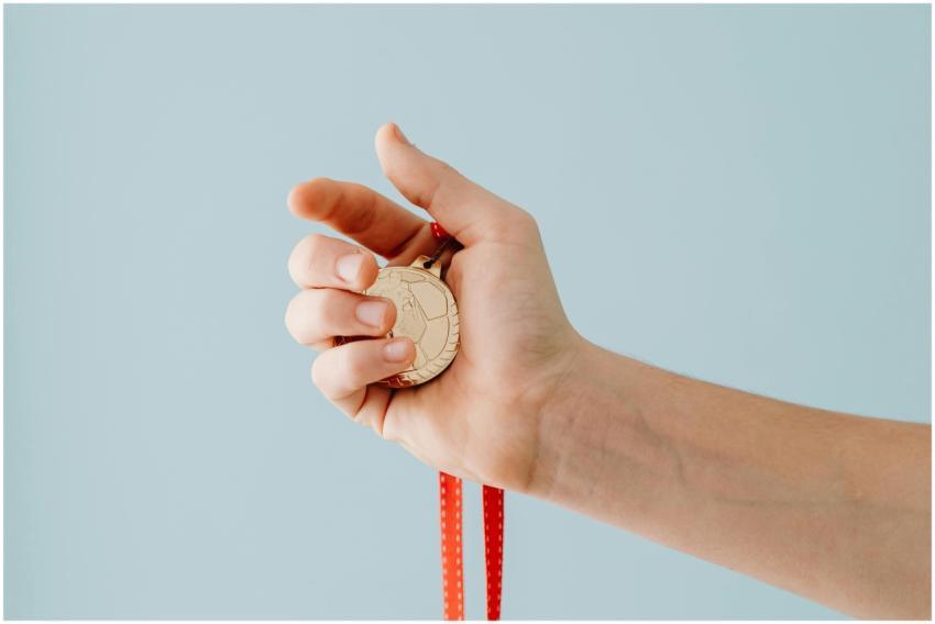 A close-up image of a hand holding a gold medal wi