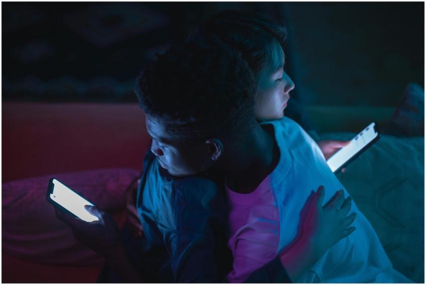 Interracial couple embracing while using smartphon