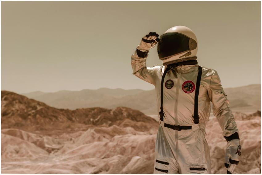 An astronaut in a silver spacesuit explores a rock