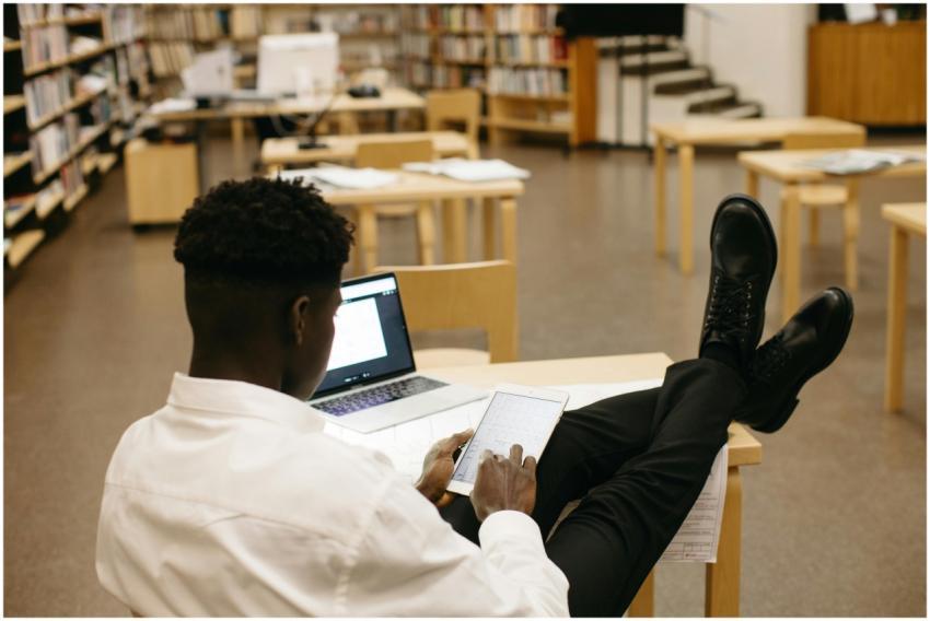 Black man studying in library with laptop and tabl