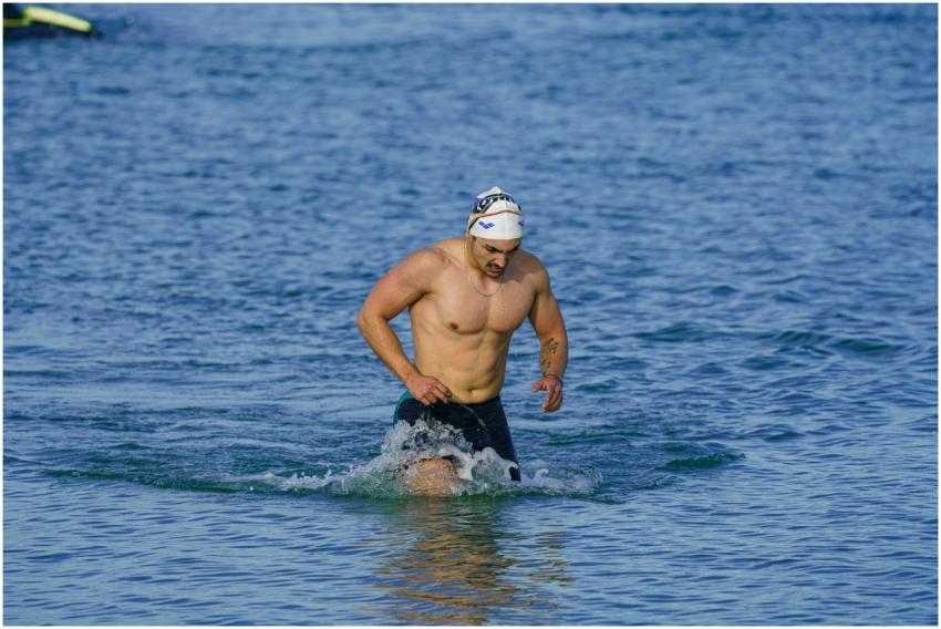 Fit adult male swimmer emerging from the sea in Ku
