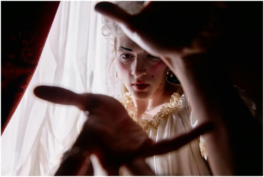 A woman in period costume with dramatic makeup pos