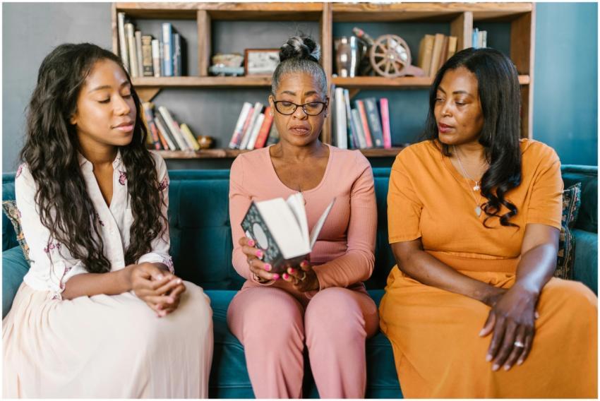 Three women sitting on a couch reading a book toge