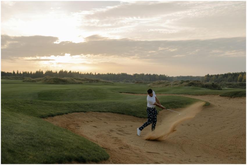 Golfer hitting a sand shot at sunset on a scenic g