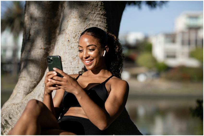 A happy woman sitting under a tree, texting on her