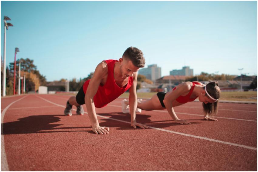 Two athletes doing push-ups on a track during dayt