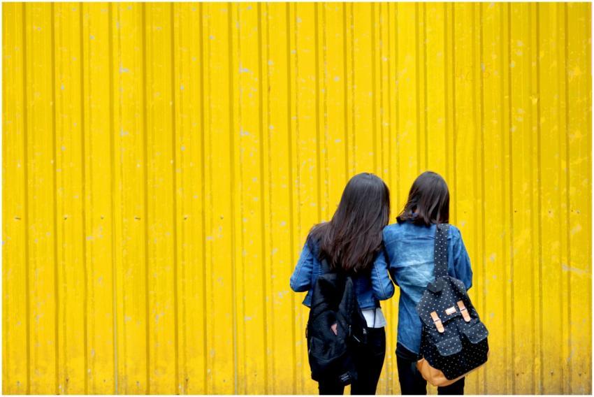 Two women wearing denim jackets and backpacks stan