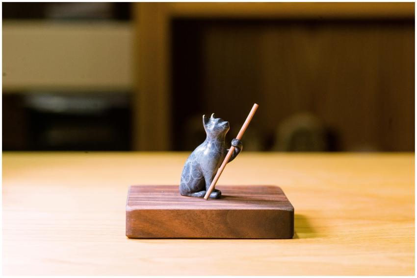 A detailed stone cat figurine holding a stick on a