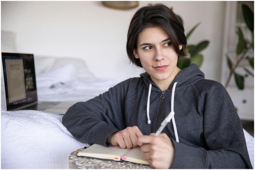 A woman in a hoodie writing in a notebook with a l