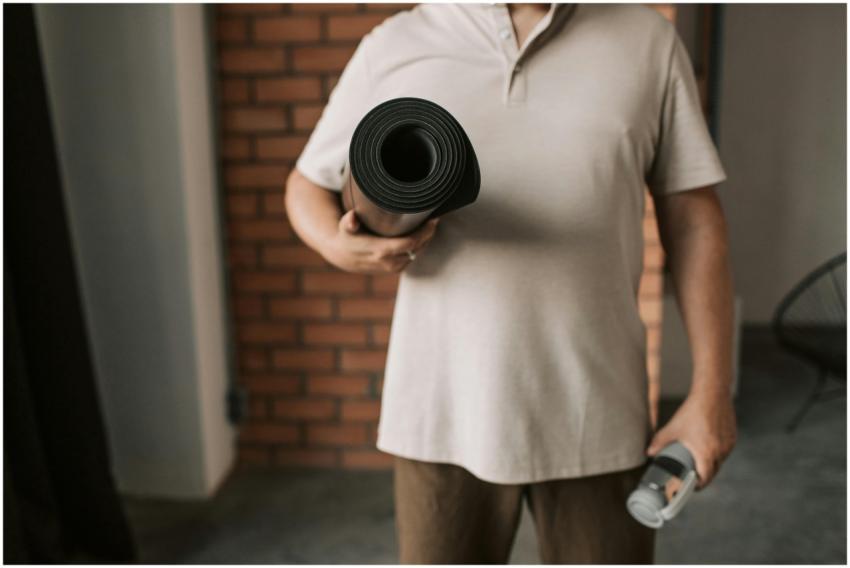 Adult man in a beige polo shirt holding a yoga mat