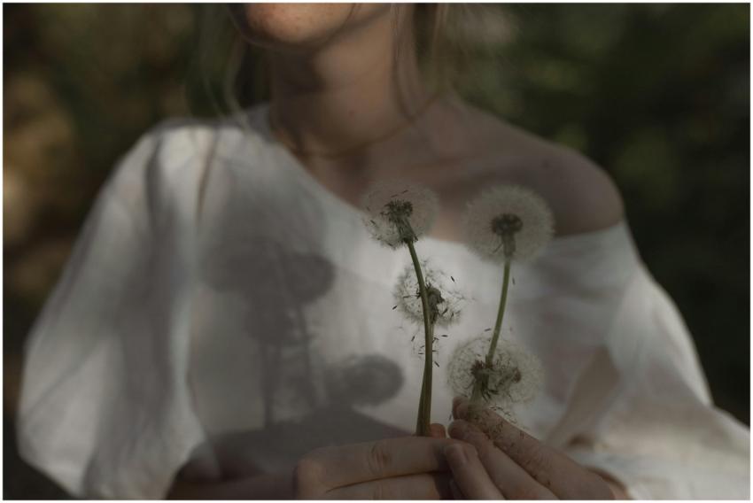 A woman in soft light holding dandelions, creating
