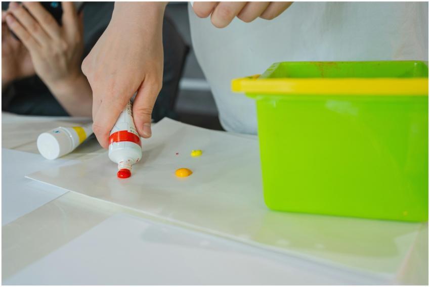 Hands squeezing colorful paint onto a sheet in a v
