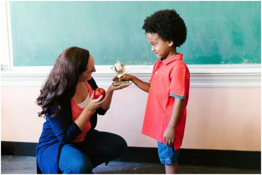 Teacher kneeling and handing a trophy to a smiling