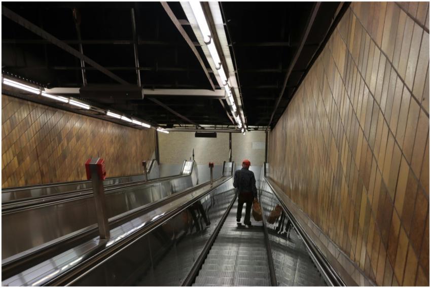 Man on escalator in Munich subway station, showcas