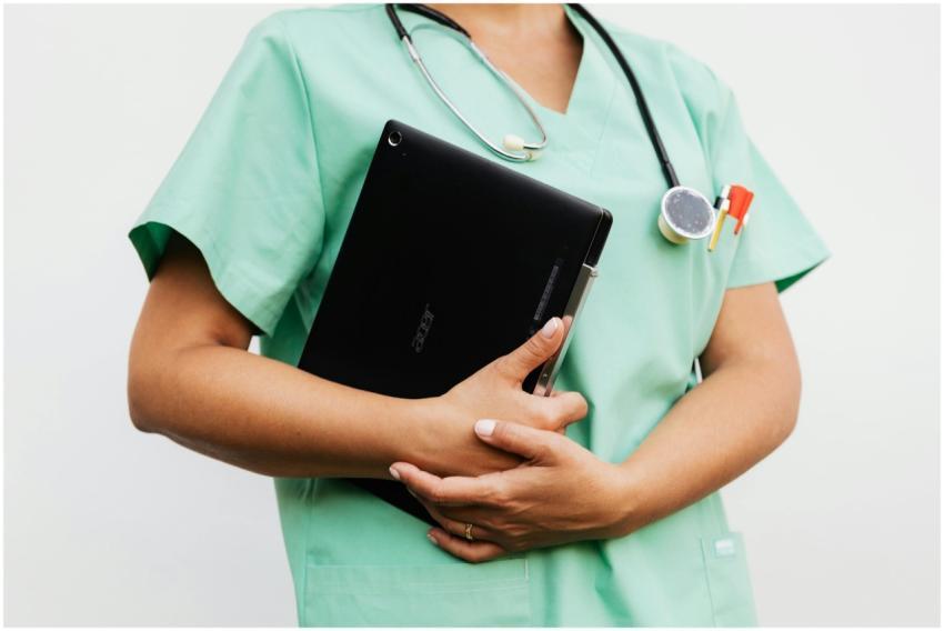 Close-up of a nurse in green scrubs holding a tabl