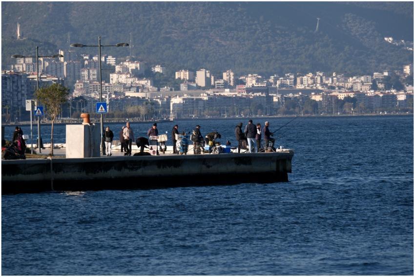 People fishing on a pier with Izmir cityscape as b