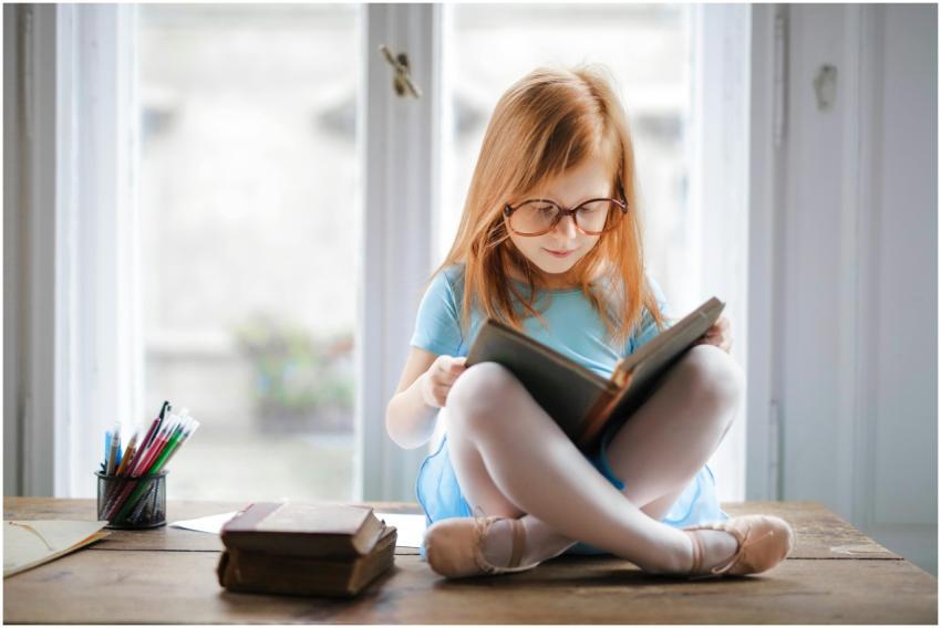 Adorable young girl wearing glasses, reading a boo