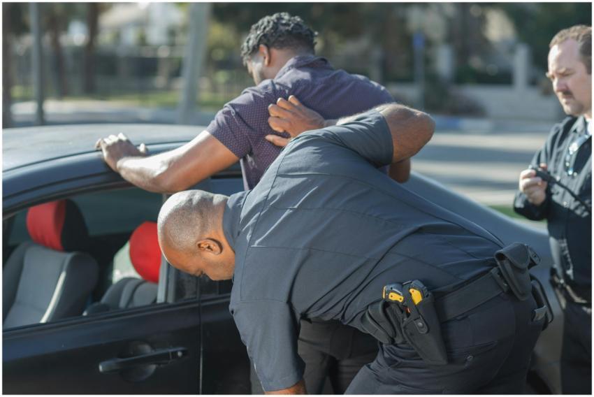 Police officers searching a suspect by a car for p