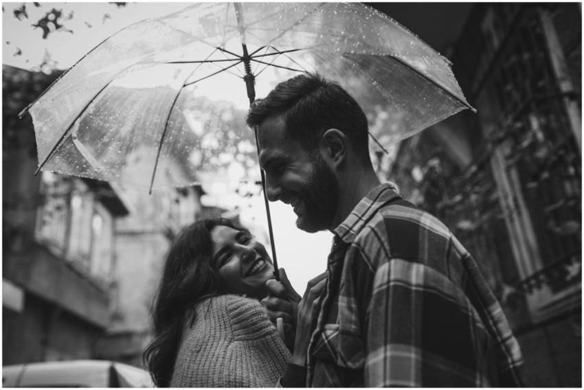 Happy couple sharing an umbrella, smiling in a rai