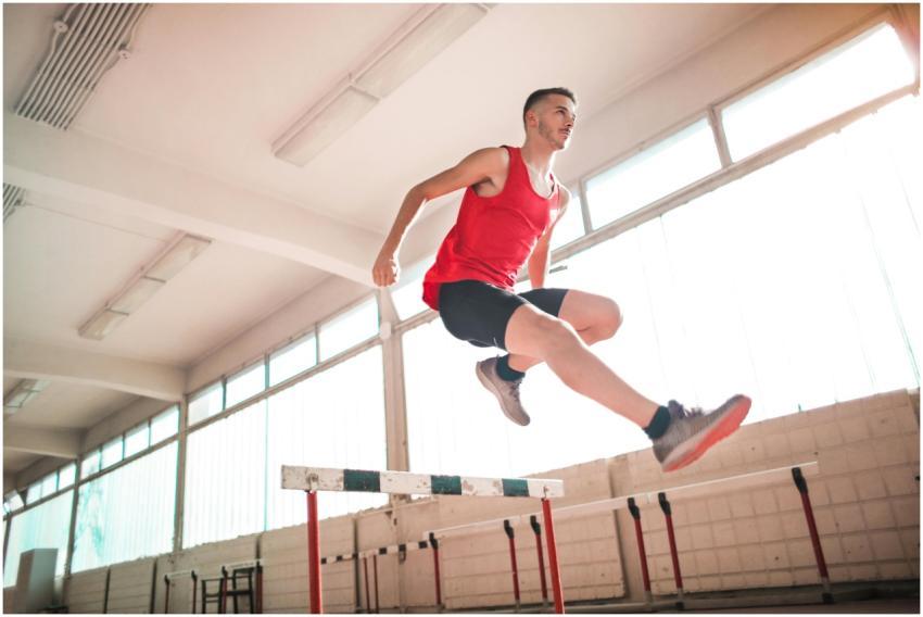 A young male athlete in a red outfit jumps over a